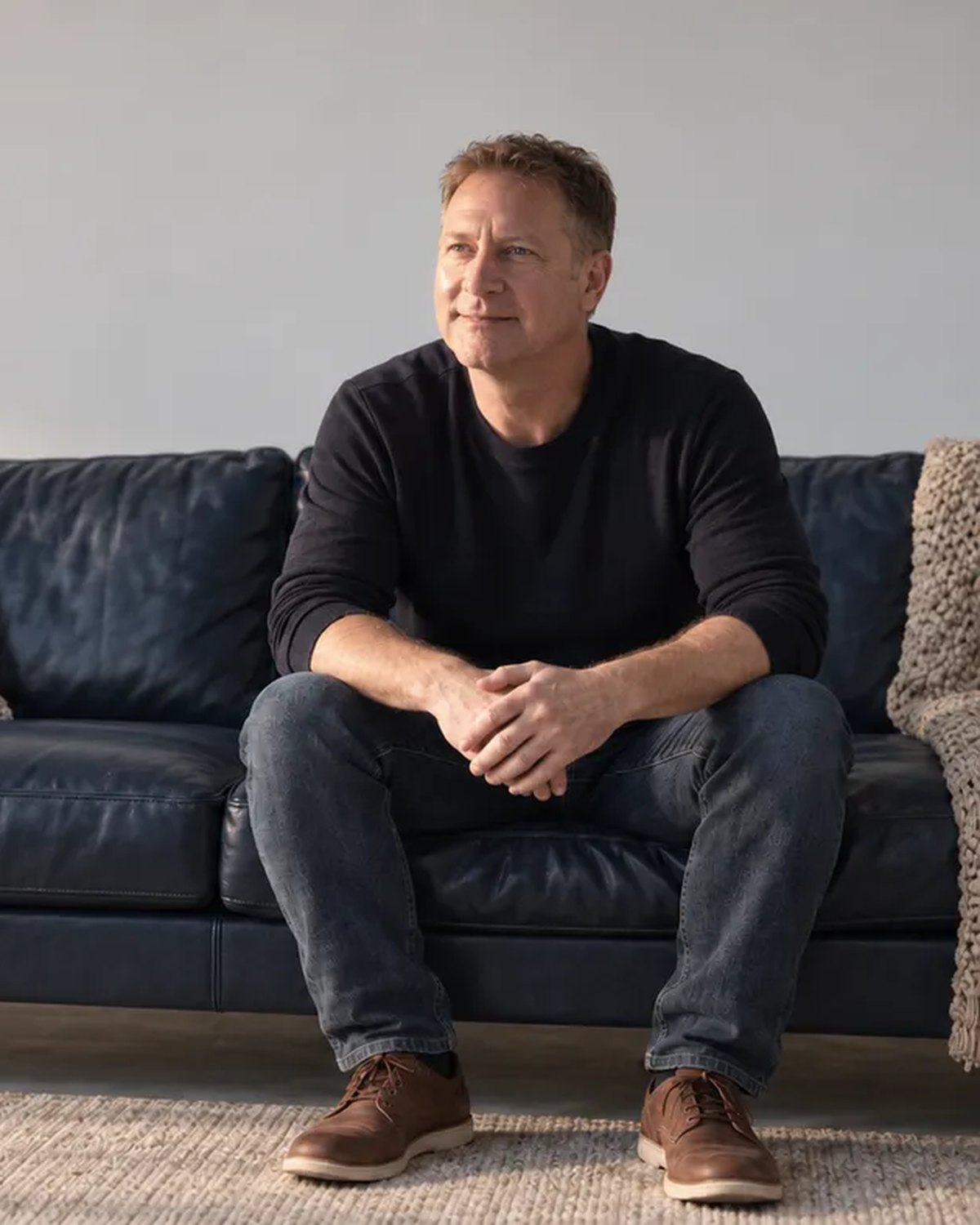 Steve Prince seated on a navy sofa in a sunlit living room