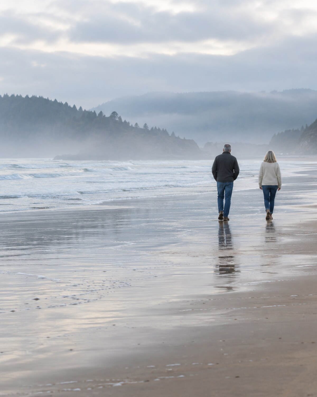 Two people seen from behind walking side by side along a wide, quiet shoreline
